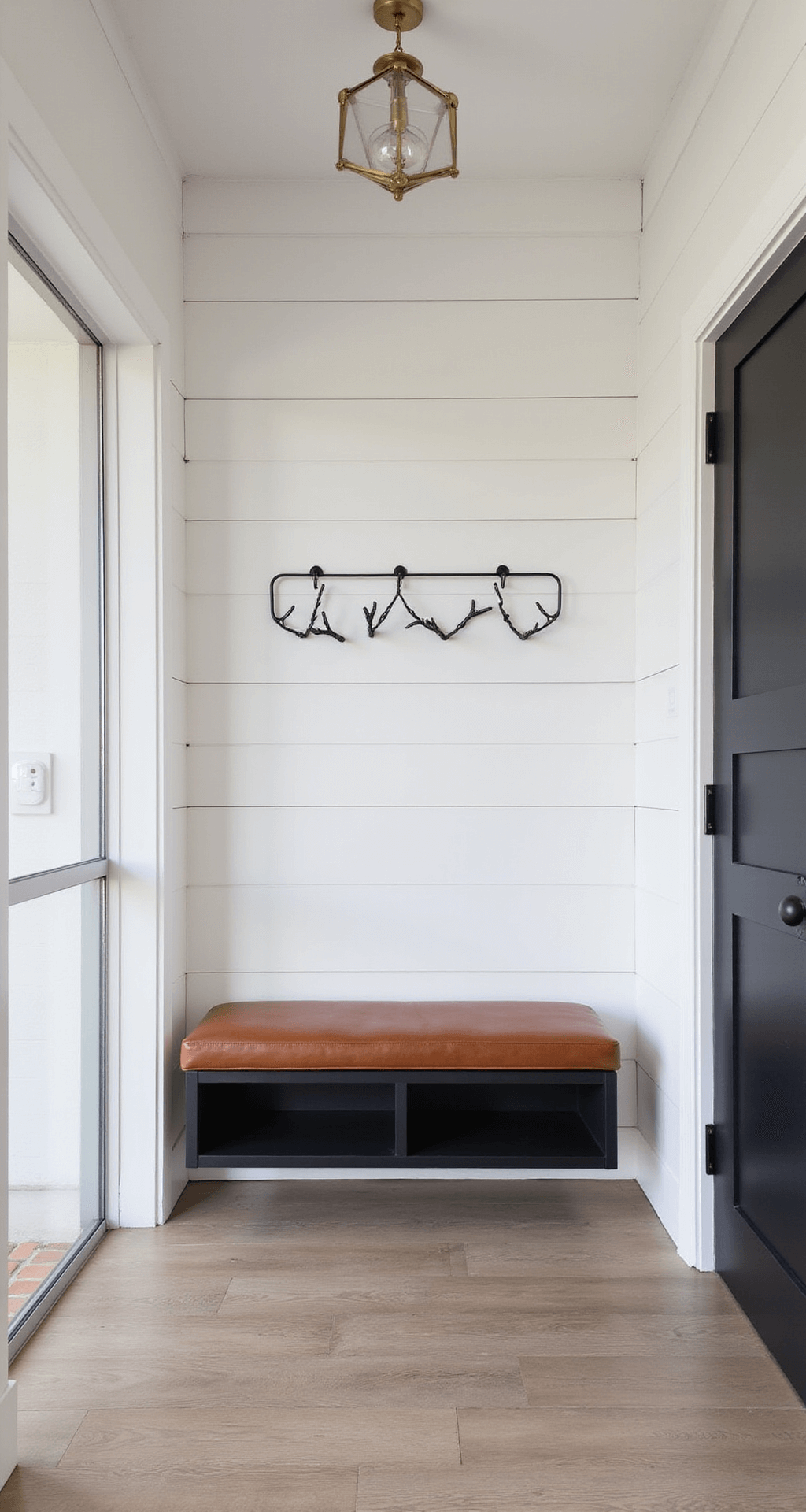 Modern foyer with white shiplap walls, black accents, floating cognac leather bench, white oak flooring, and geometric brass pendant light.