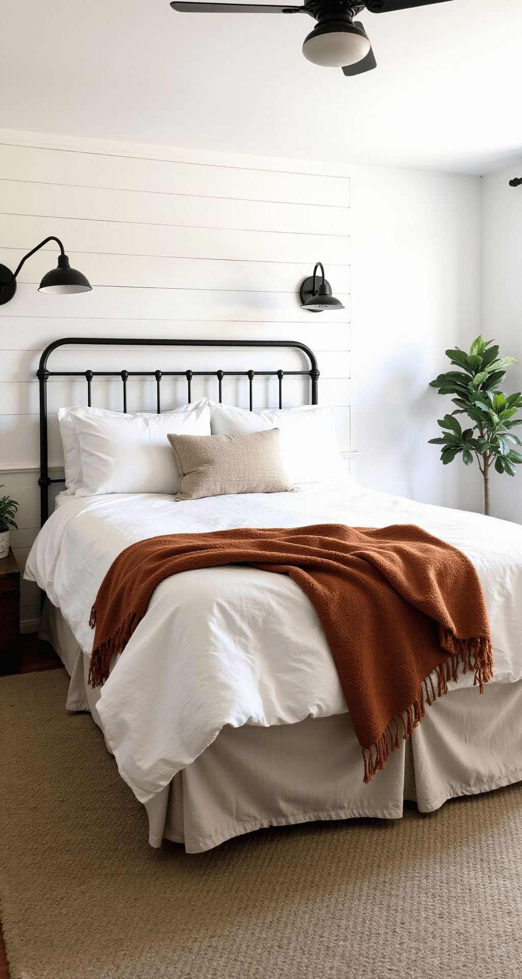 Modern farmhouse guest room featuring a shiplap accent wall, iron bed with oatmeal Belgian linen duvet, autumn rust handwoven throw, black metal sconces, vintage trunk luggage rack, and fiddle leaf fig, photographed in natural midday light.