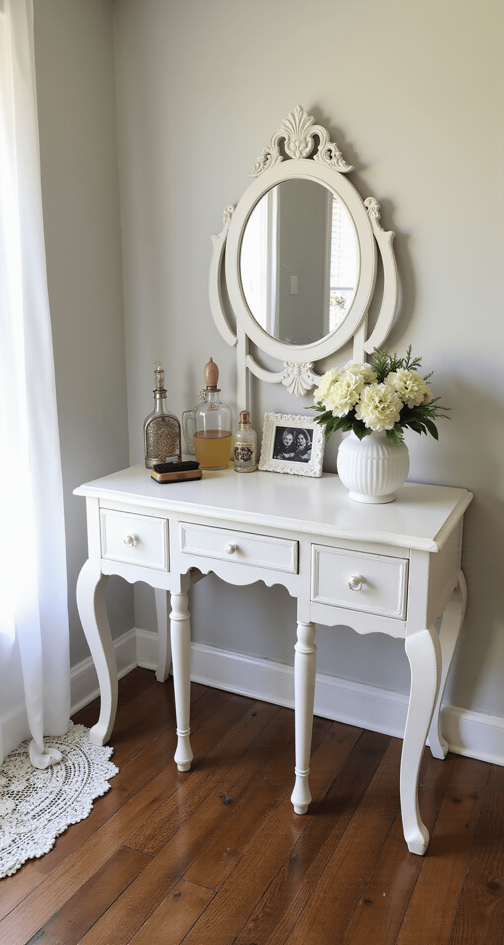 A beautifully styled guest bedroom corner featuring a white chalk-painted French provincial vanity with an original mirror, vintage perfume bottles, a silver brush set, and fresh flowers in a milk glass vase, all illuminated by mid-morning light. Delicate lace doilies and family photographs add personal touches, captured from a 45-degree angle to showcase textures and surface details.