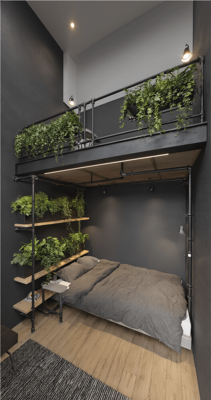 Dramatic dusk shot of a tall bedroom featuring a charcoal gray accent wall with cascading wall planters, a loft-style bed with workspace below, and industrial pipe shelving, captured from a low angle to emphasize height and moody ambient lighting.